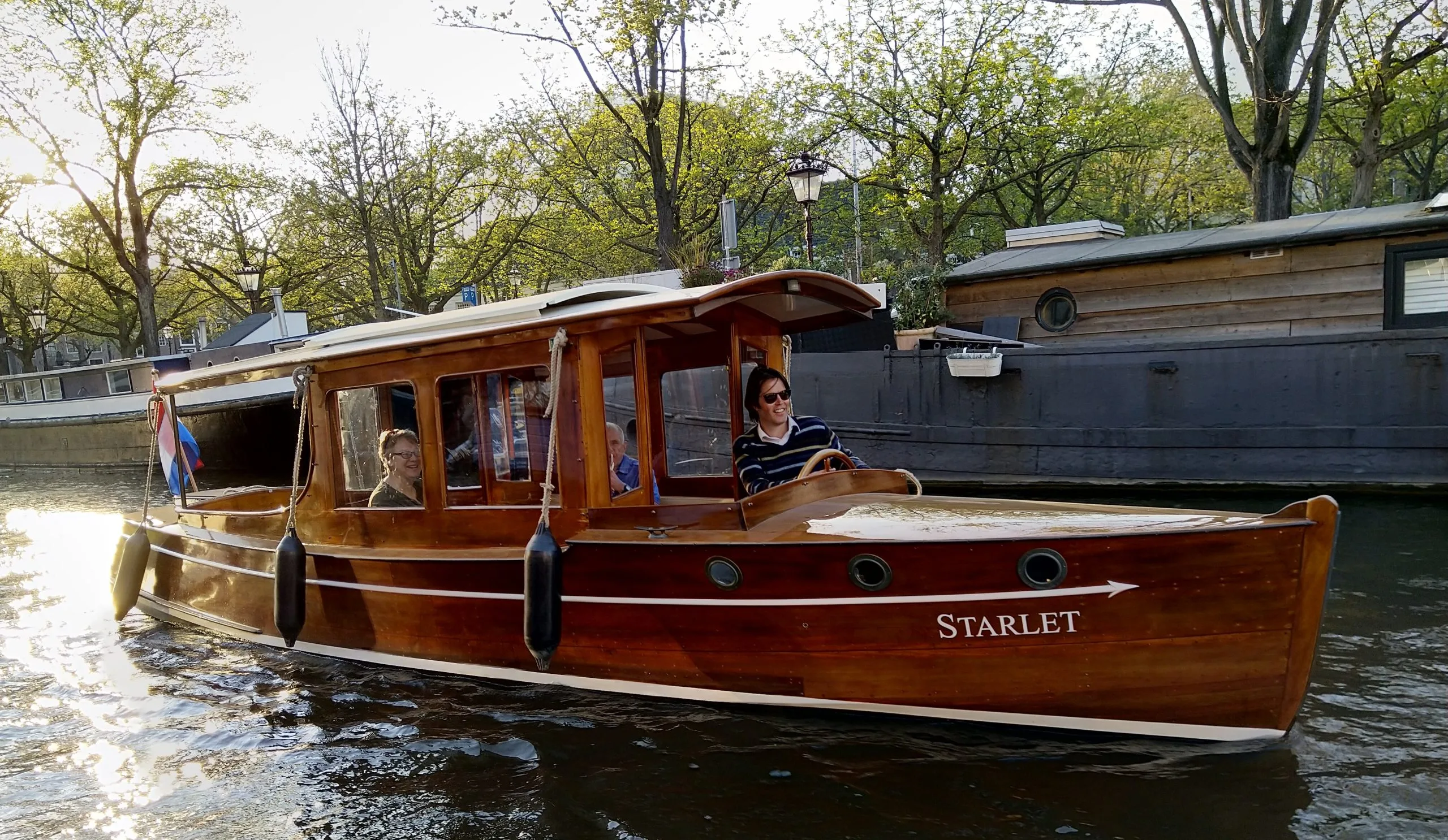 Klassieke houten salonboot 'Starlet' met passagiers, varend op een gracht tijdens een zonnige avond.