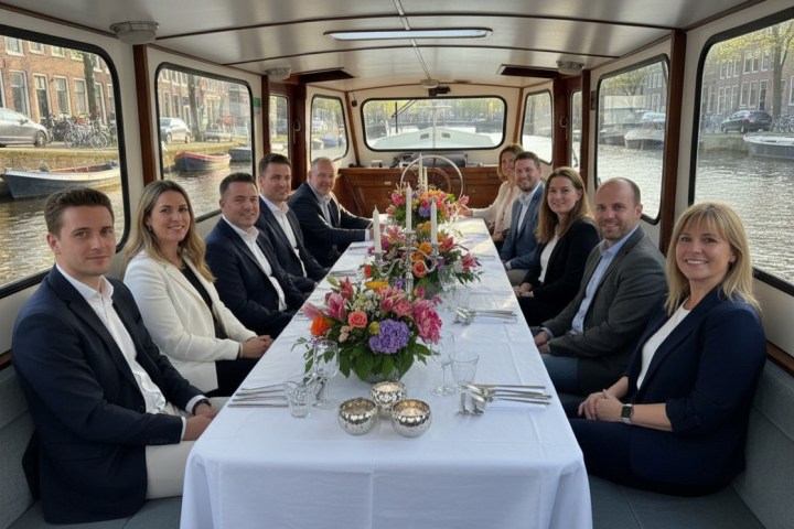 Group of people seated at a dinner table on a boat with floral centerpiece.