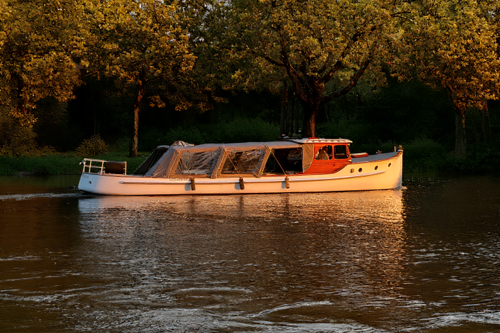 White boat with canopy on calm river surrounded by trees.