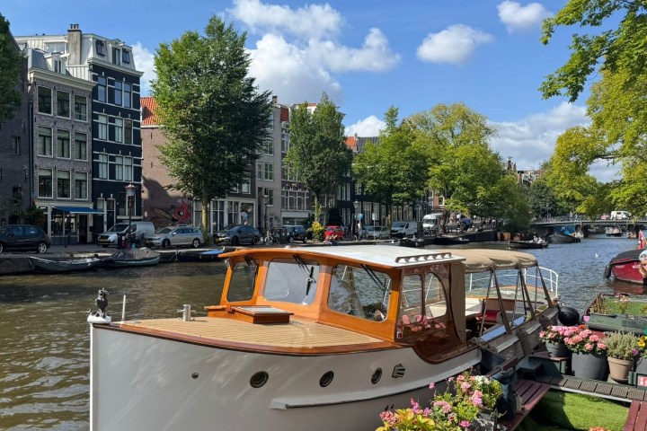 Wooden boat docked on a canal with historic buildings and trees in the background.