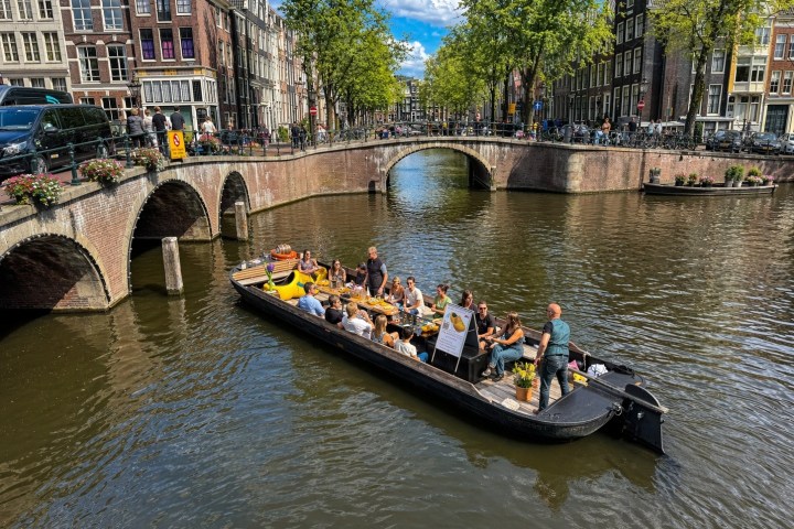 Canal with boat of people passing under bridges in a city with historic buildings.