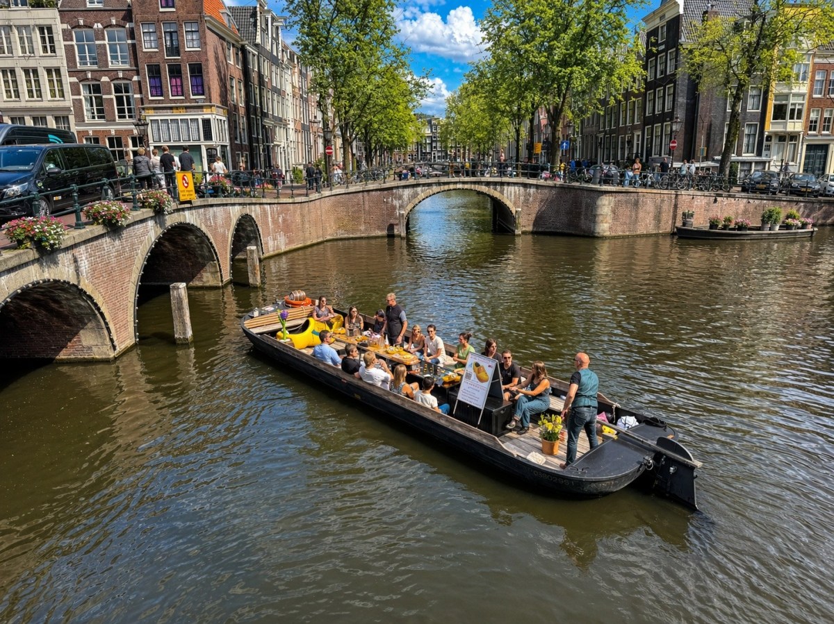Canal with boat of people passing under bridges in a city with historic buildings.