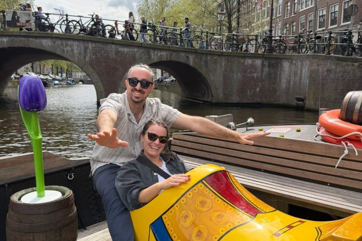 Two people in a giant yellow clog by a canal with a tulip sculpture nearby.