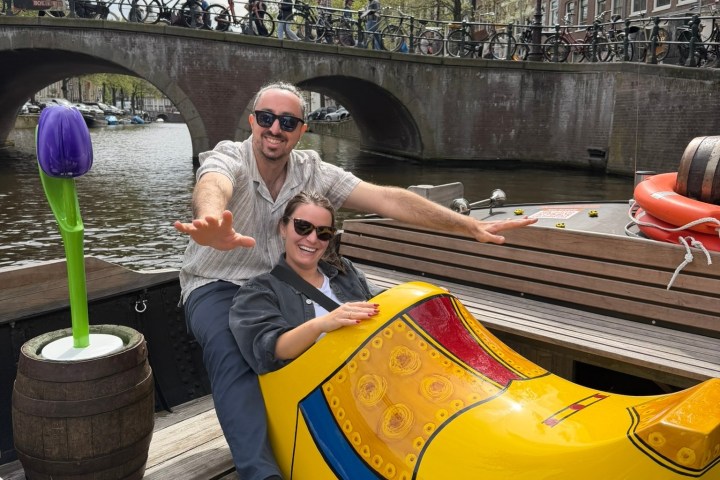 Two people in a giant yellow clog by a canal with a tulip sculpture nearby.