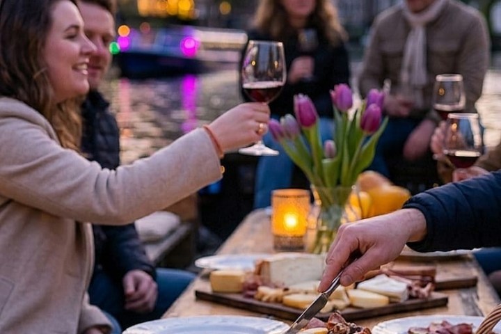 People enjoying an outdoor meal with wine by a canal, wooden clogs as food trays, tulips on table.