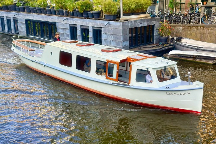 White canal boat named LEEMSTAR V on a waterway with potted plants on the dock.