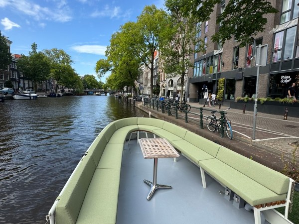 Boat with green seats on canal, red carpet, trees and buildings lining the water.