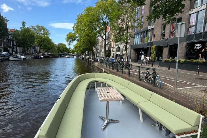 Boat with green seats on canal, red carpet, trees and buildings lining the water.