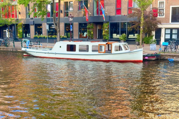 White canal boat moored alongside a canal with colorful brick buildings.