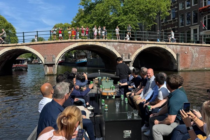 People seated on a boat in a canal under a bridge with sunny skies.