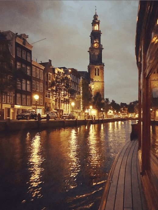 Canal at dusk with lit streetlights and tall clock tower reflecting in water.