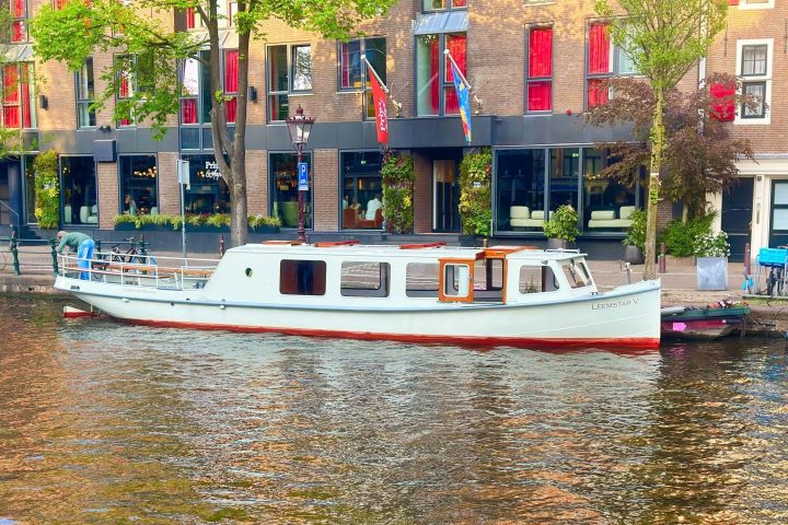 White boat moored on canal with brick building and trees in background.