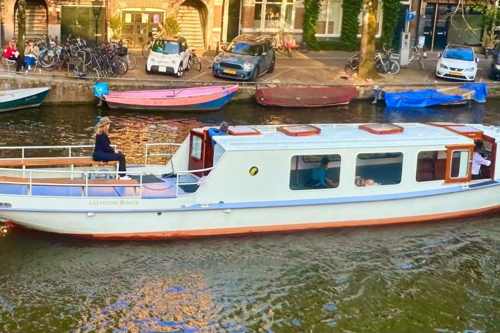 White boat on canal with person seated, buildings in background.