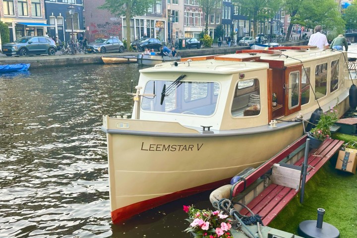 Boat named Leemstar V docked along a canal in a city with buildings and trees.