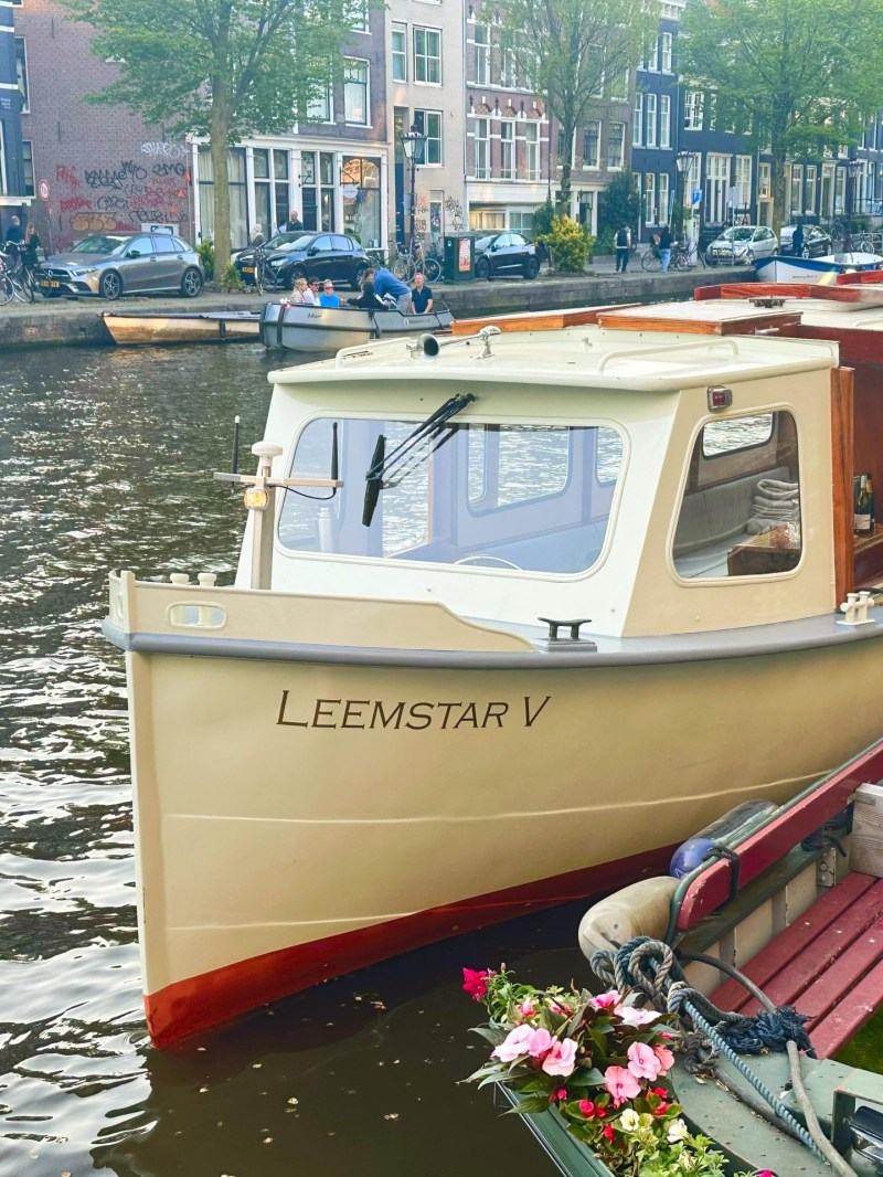 Boat named Leemstar V docked along a canal in a city with buildings and trees.