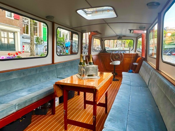 Interior of a boat with seating, table, ice bucket, and outdoor canal view.