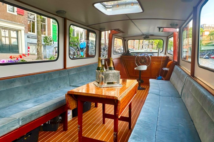 Interior of a boat with seating, table, ice bucket, and outdoor canal view.