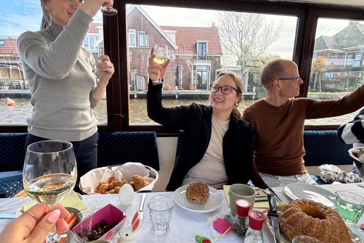 Three people on a boat raising glasses in a toast with food on the table.