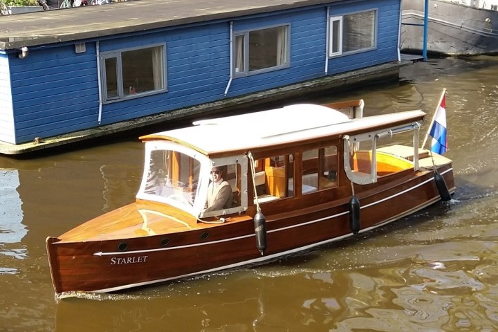 Wooden boat with a Dutch flag on a canal near a blue houseboat.