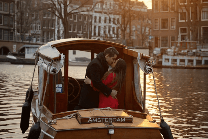 Couple embracing on a Leemstar Cruises boat in Amsterdam canal at sunset.