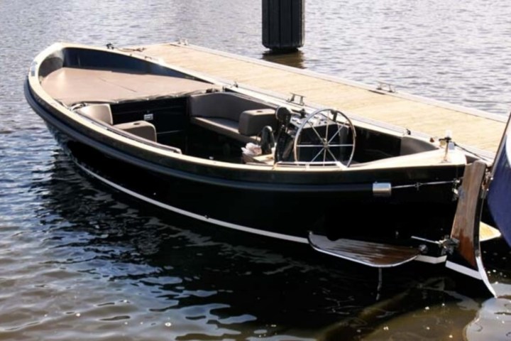 Sleek black boat docked beside a pier, with a flag at the stern.