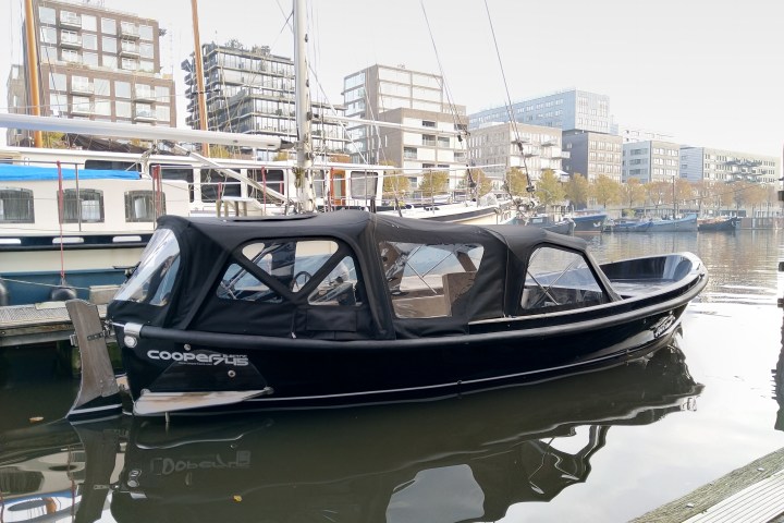 A black boat docked at a marina with city buildings in the background.