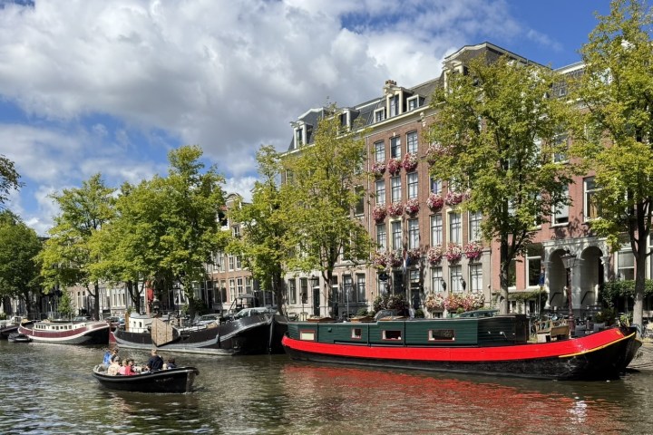 Canal with boats, tree-lined street, and historic buildings under a cloudy sky.