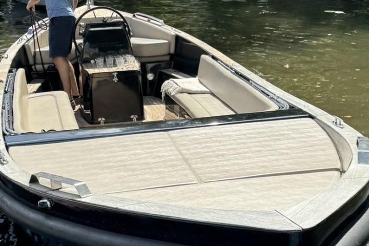 Person standing in a sleek black yacht with beige seating on a calm waterway.