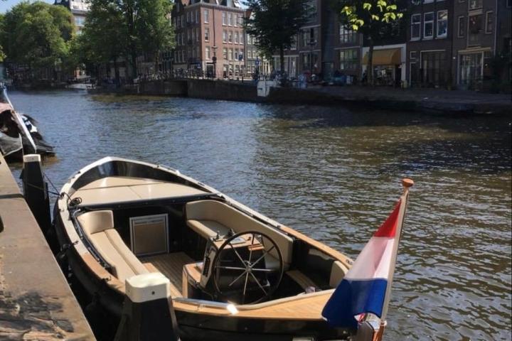 Boat docked in a canal with buildings and trees in the background.
