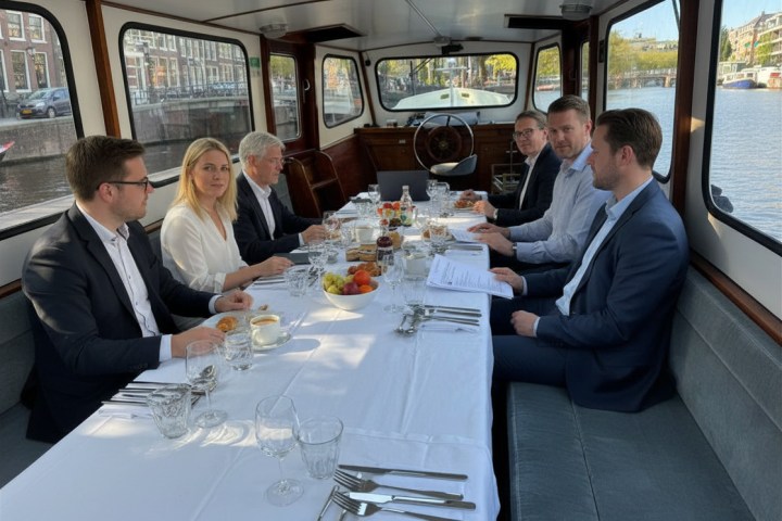 Six people in formal attire having a meeting on a boat with a set dining table.