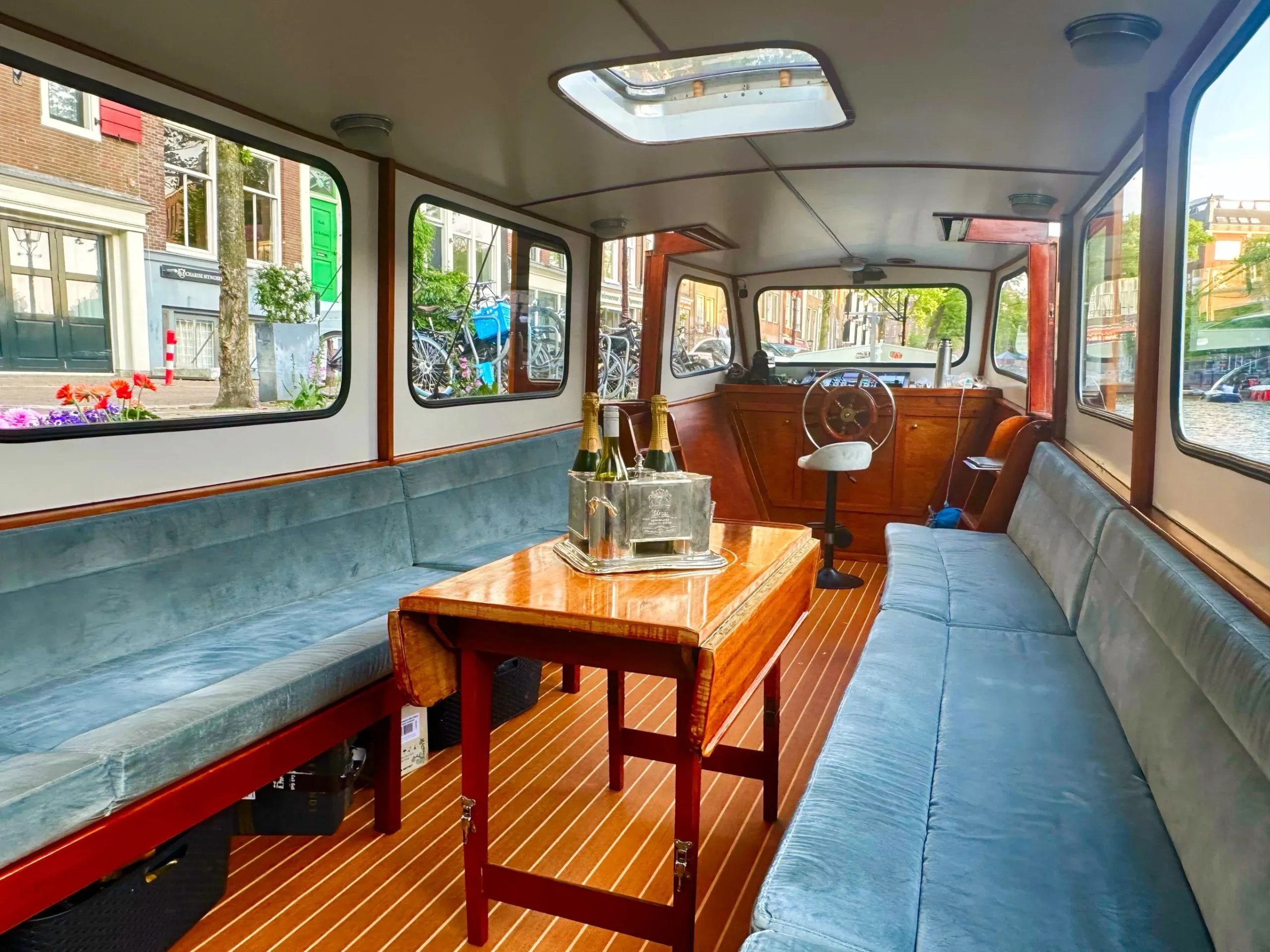 Interior of a boat with blue seating, wooden table, and champagne bottles.
