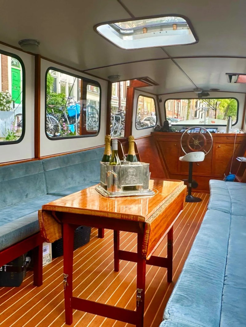 Interior of a boat with blue seating, wooden table, and champagne bottles.