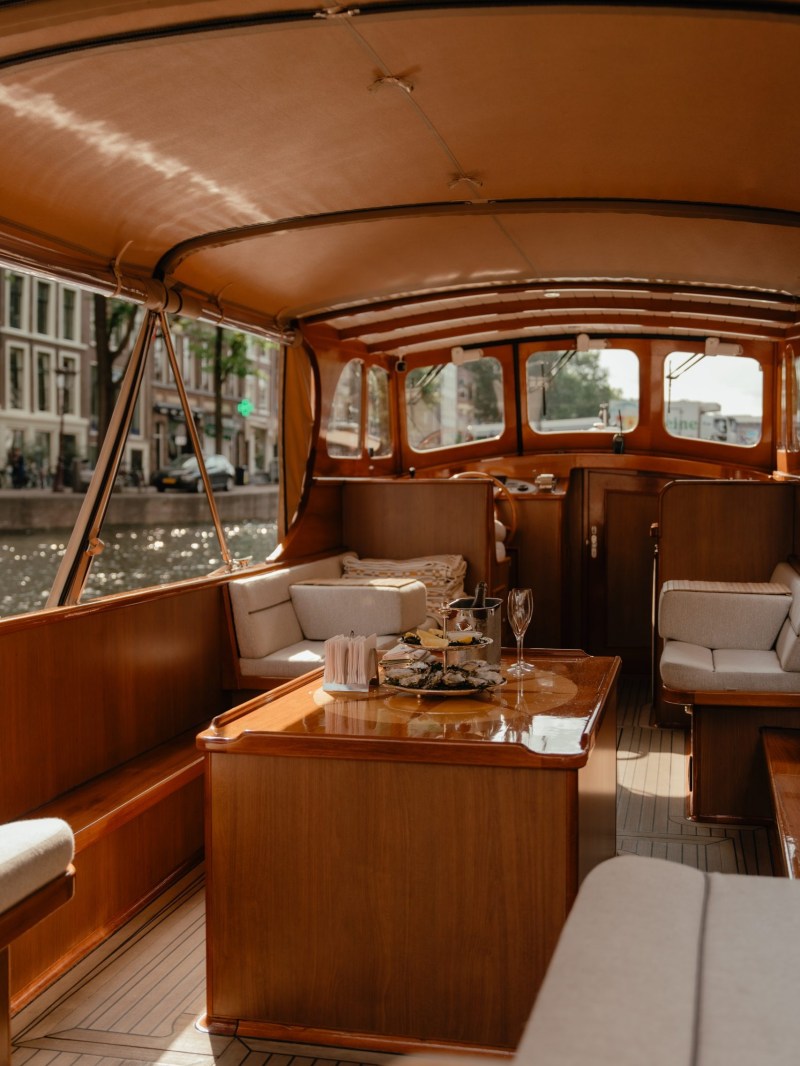 Interior of a boat with wooden furniture and cushions on a sunny day.