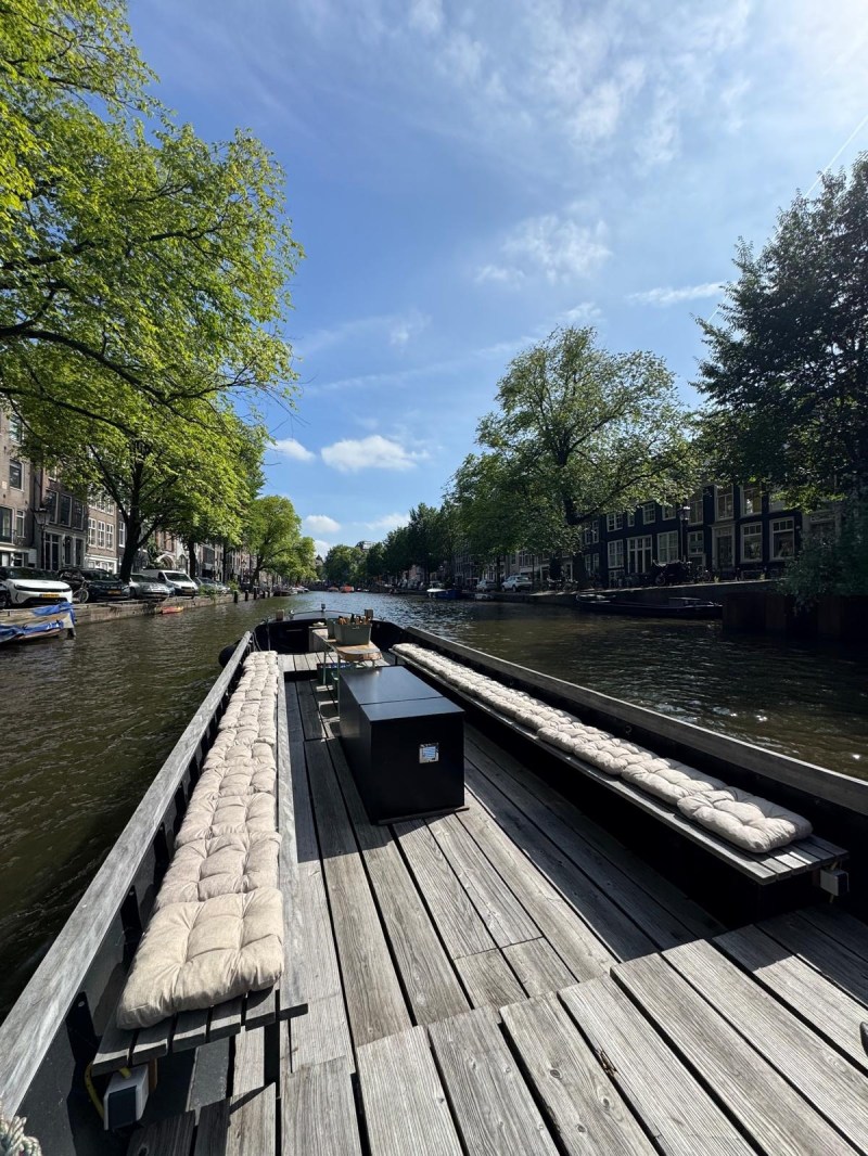 Empty boat with cushioned seats on canal under blue sky with trees lining the waterway.