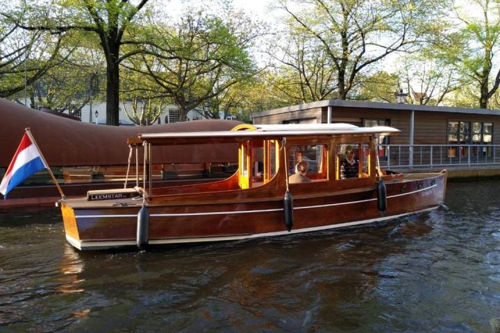 Wooden canal boat with Dutch flag on water, surrounded by trees.
