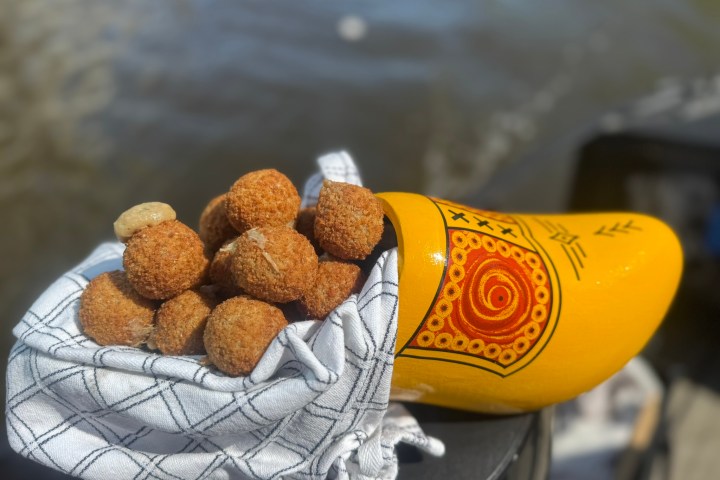 Yellow wooden shoe filled with croquettes on a checkered cloth by a riverside.