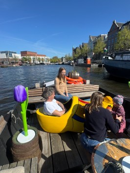 People sitting in large yellow clog boat on canal, bright day.