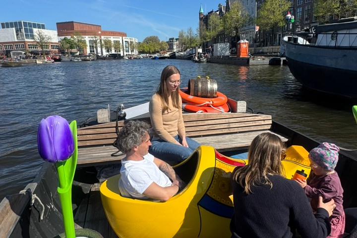 People sitting in large yellow clog boat on canal, bright day.