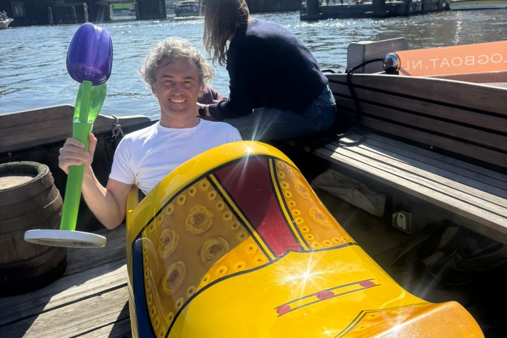 Person in giant yellow clog holding inflatable tulip by water.